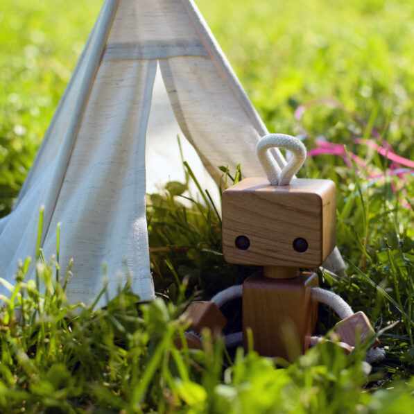 Wooden robot toy and tipi tent toy in the grass.