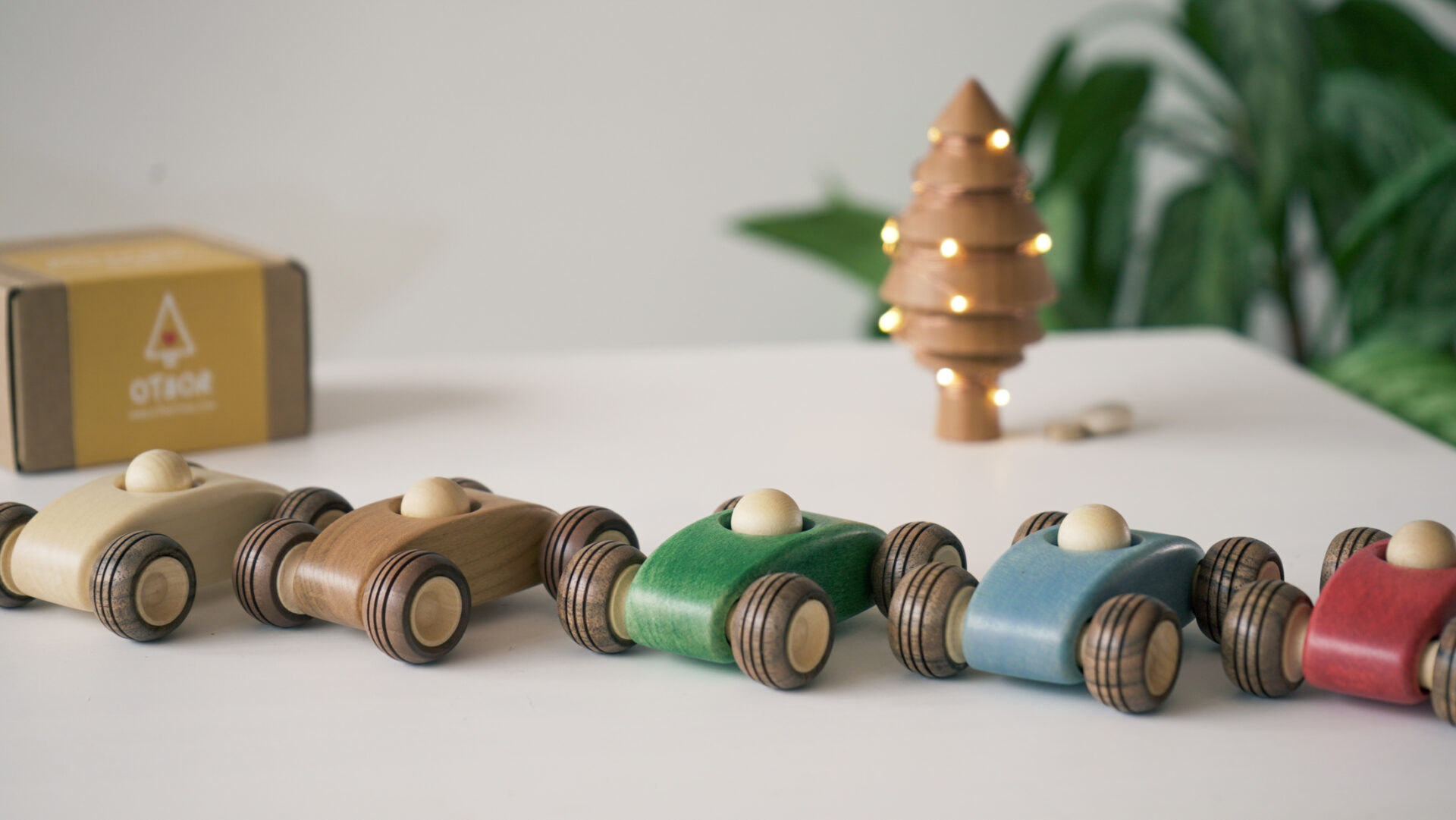 10 Christmas Gift Ideas for Toddlers (No Batteries Needed!) 5 Row of handcrafted wooden toy cars displayed in a festive setting with Christmas lights and a decorated tree — ideal holiday gifts for curious toddlers.