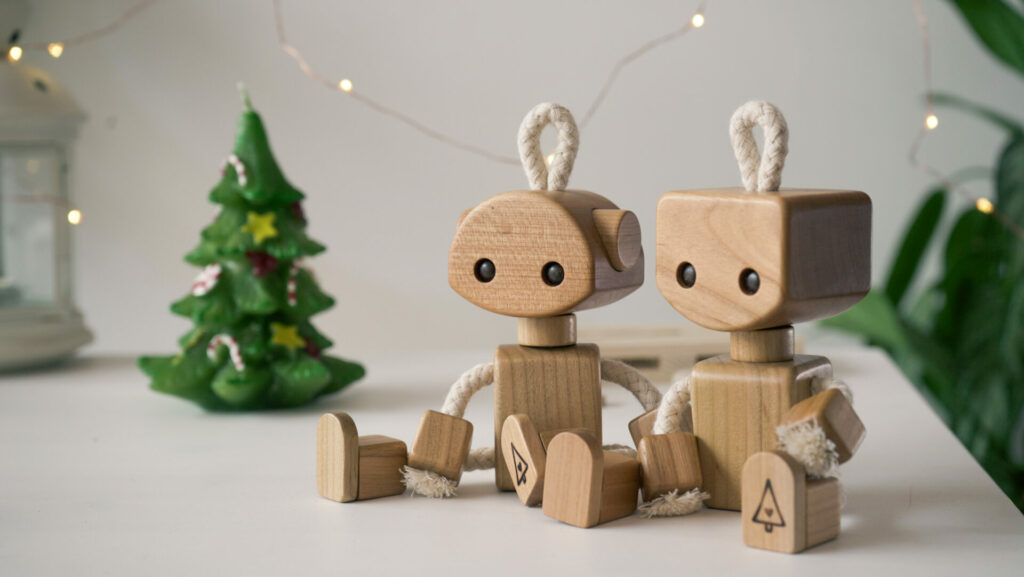 10 Christmas Gift Ideas for Toddlers (No Batteries Needed!) 2 Two handmade wooden robots in front of Christmas lights and a decorated tree — perfect screen-free Christmas gift ideas for toddlers.